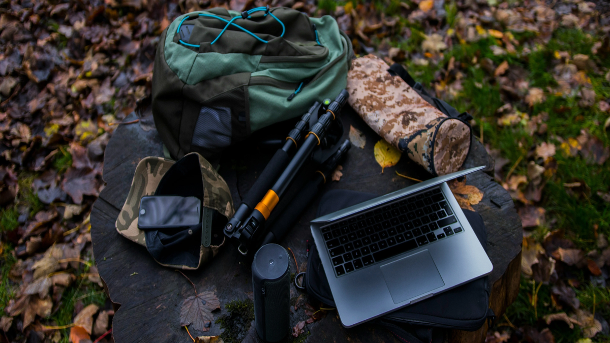 Laptop, phone, backpack and hiking poles arranged on a woodland picnic table.